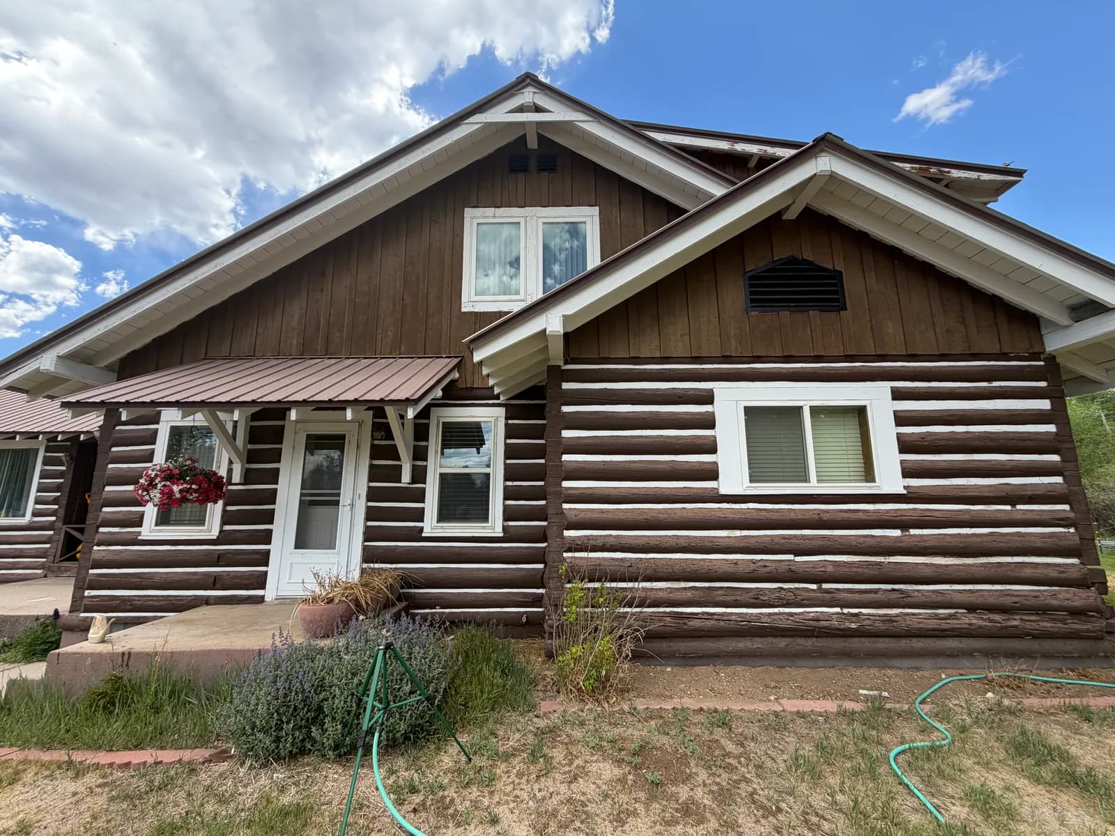 Historic dark-stained log home with white mortar-style chinking lines, a craftsman gable, and a covered porch in Colorado