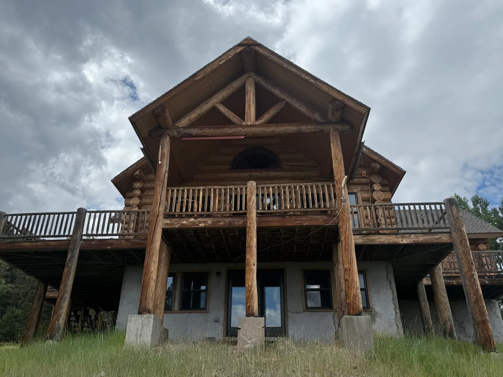 Massive round log posts supporting an elevated log home deck above a stucco lower level, freshly finished, on a Colorado mountain property