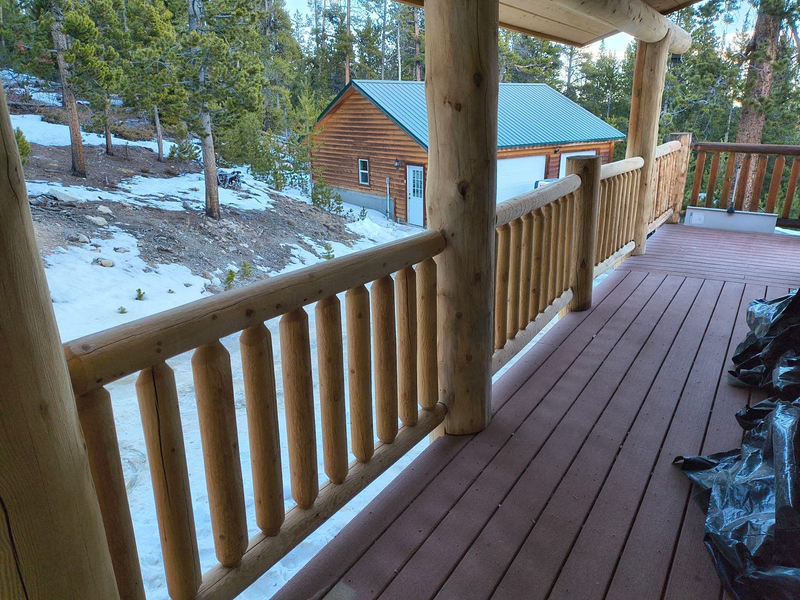 Custom log railings on mountain deck overlooking Colorado pine forest with snow-covered landscape