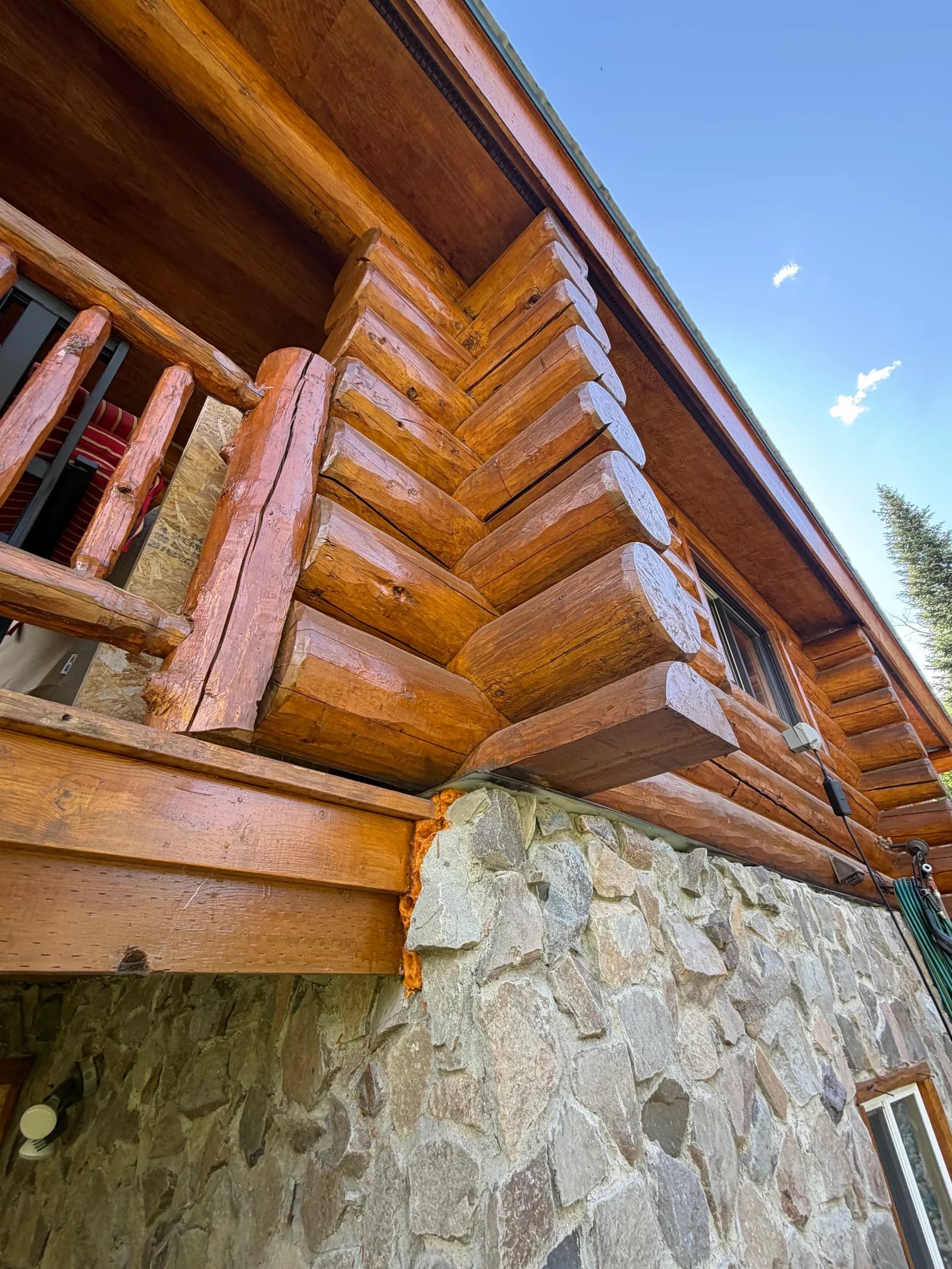 Log Home Inspection Detail — Failing Chinking Joint Close-up of log corner joinery and a roof eave above a stone foundation with a failed, separating chinking joint found during a Colorado log home inspection