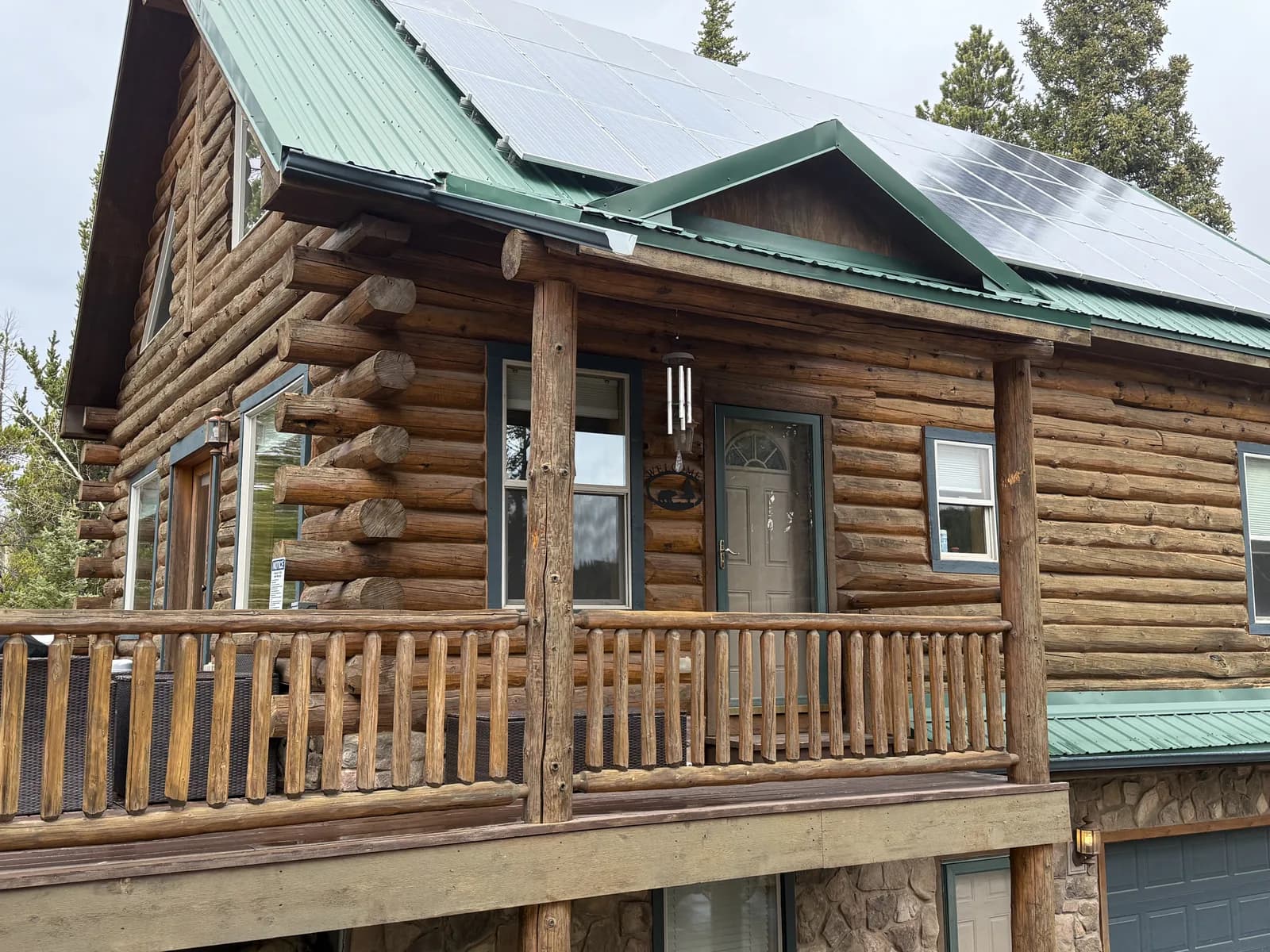 Full-Scribe Log Home — Stained & Protected Full-scribe log home with a green metal roof and rooftop solar panels above a freshly stained log facade and covered porch in the Colorado high country