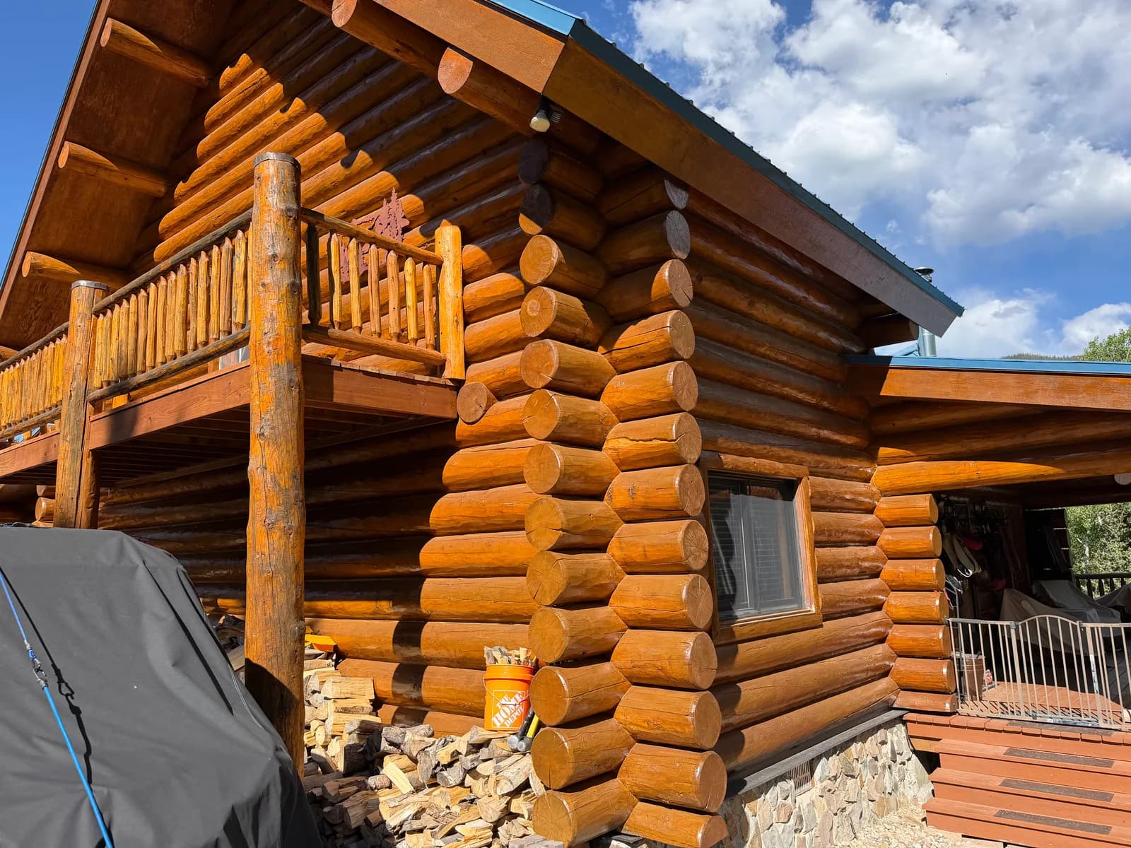 Log Home Restoration & Staining Restored full-round log home corner with a warm honey stain, a stone foundation, and a blue metal roof in the Colorado high country