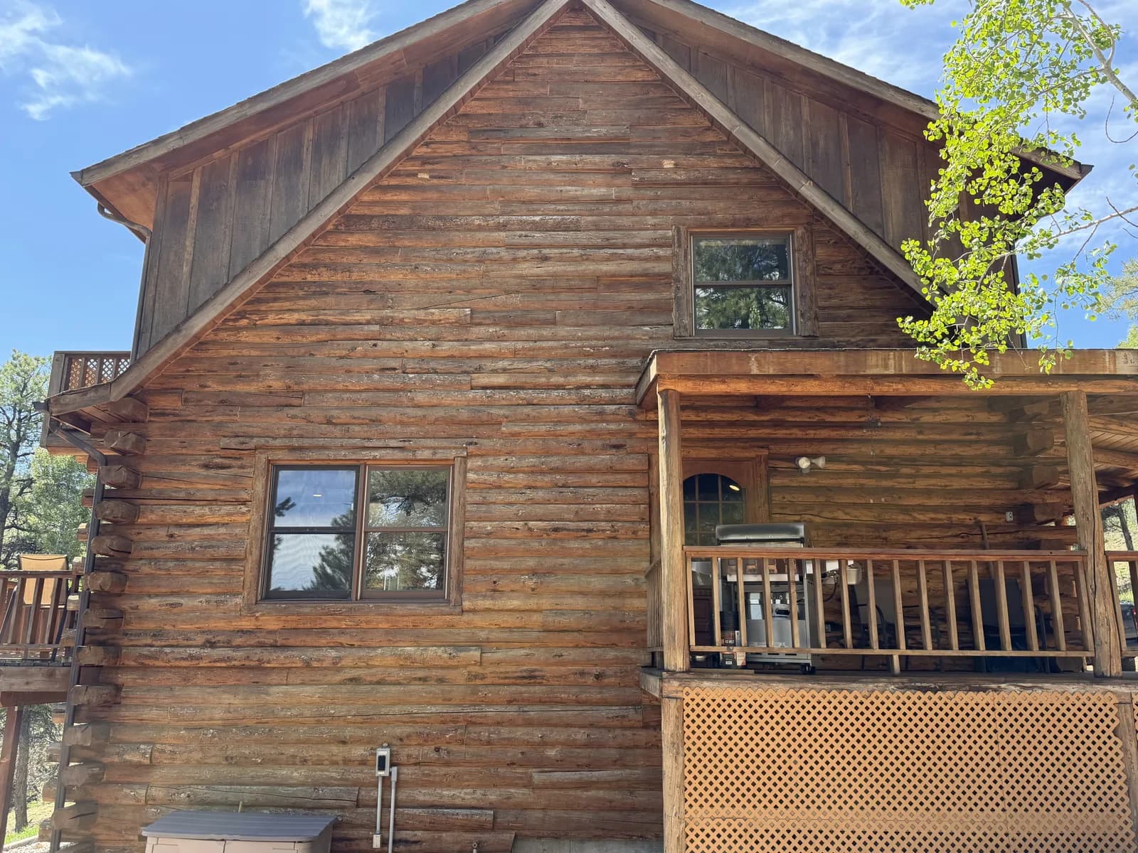 Weathered Wood Finish Before Refinishing Tall log and wood-sided building with a weathered, sun-faded finish and a covered porch under a blue Colorado sky, awaiting refinishing