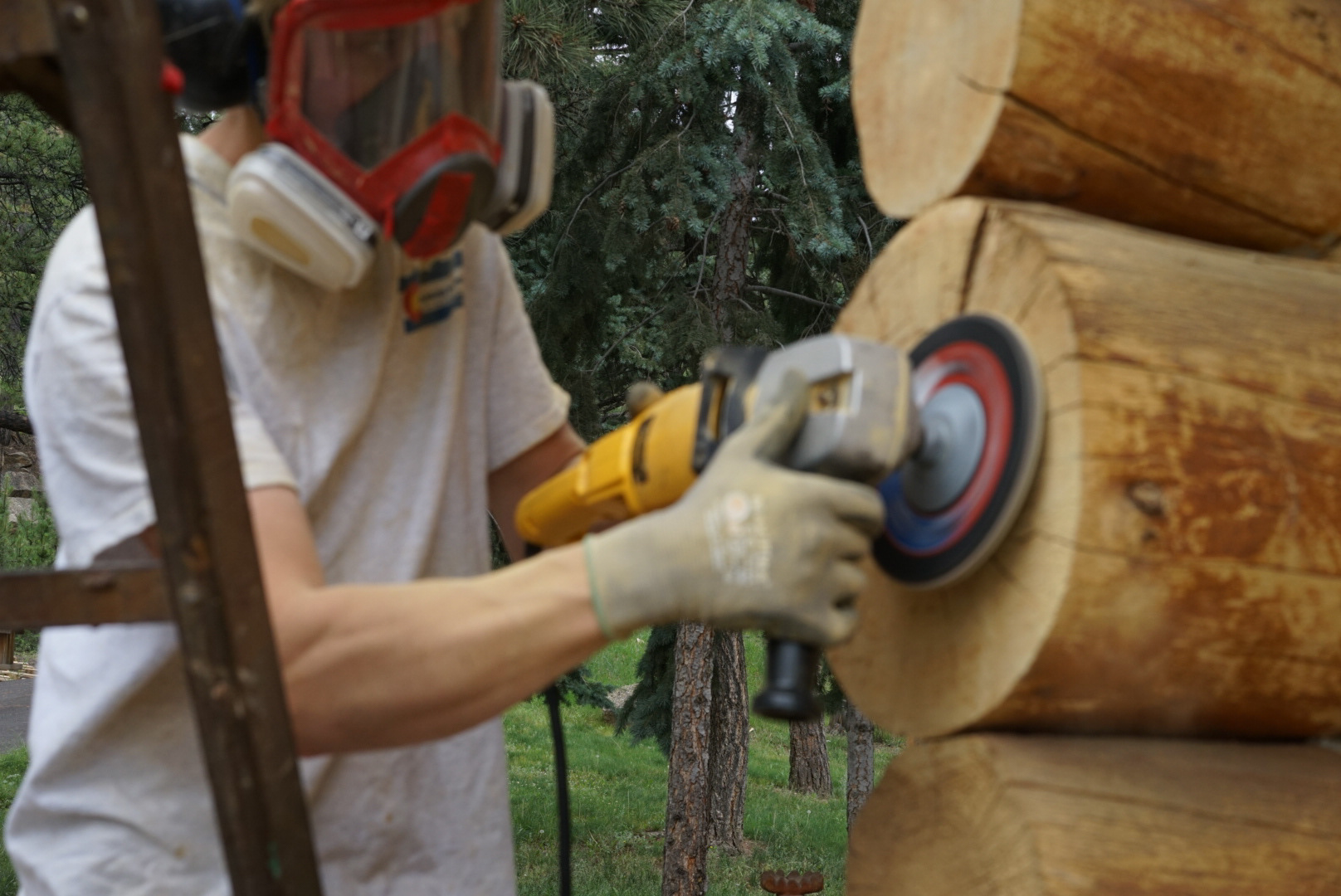 Professional log restoration specialist using grinding equipment to prepare log surface for staining