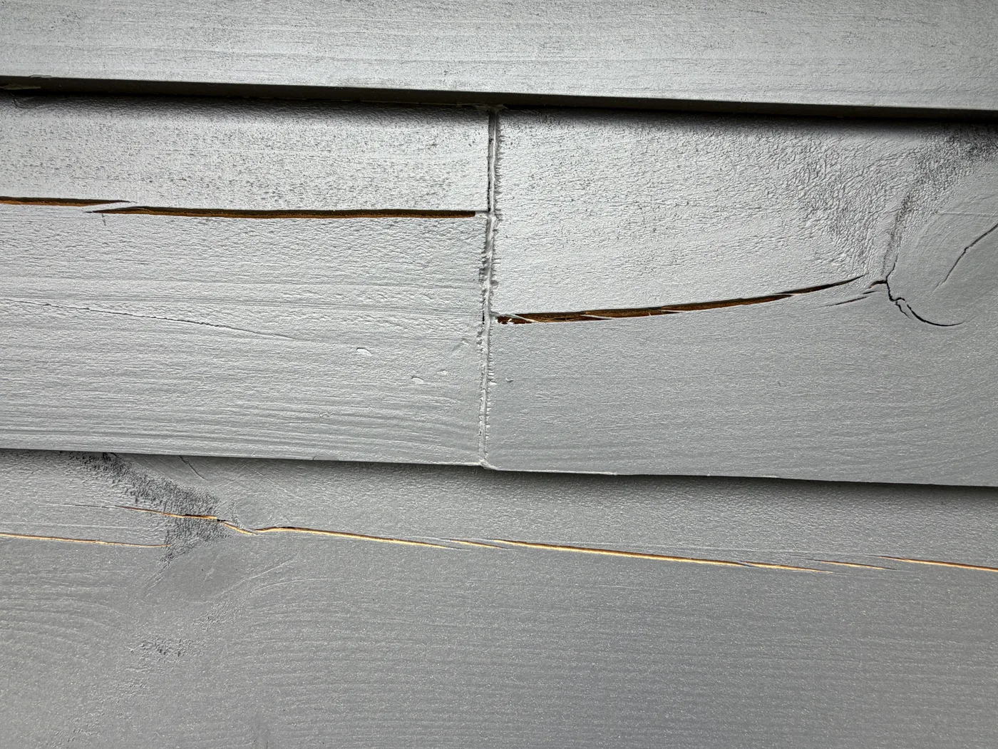 Long horizontal checking cracks splitting along the grain of grey log siding and running out of a vertical butt joint