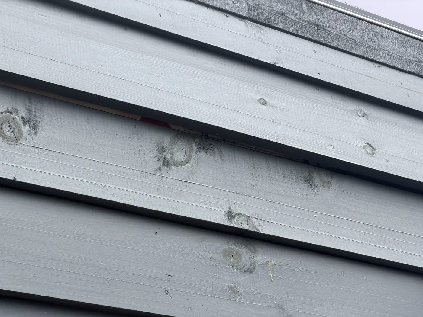 Dark mildew and moisture staining around knots and along the lower edges of grey log siding boards next to an open lap exposing the sheathing behind