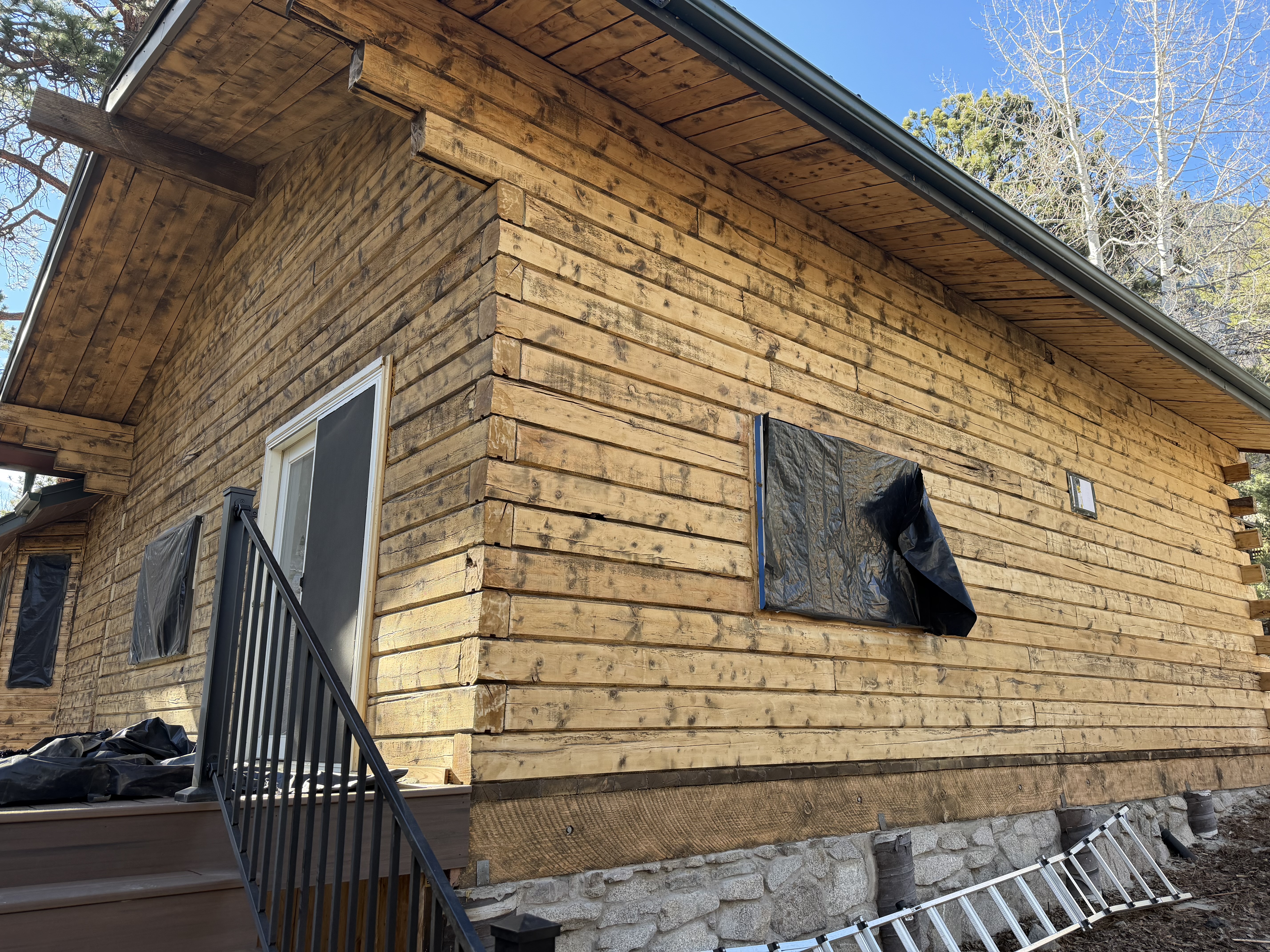 Log home during restoration in Nathrop Colorado showing bare wood after media blasting removed old brown paint - windows masked for protection