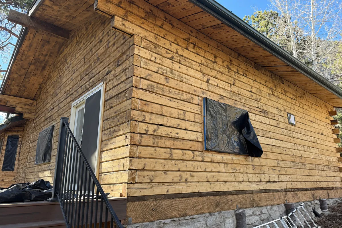 Log home during restoration in Nathrop Colorado showing bare wood after media blasting removed old brown paint - windows masked for protection