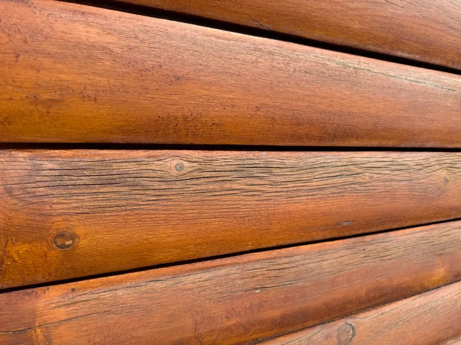 Close-up of log home exterior showing deep check cracks and weathered grain pattern on round logs — the type of surface that is extremely vulnerable to pressure washing damage, where high-pressure water can blast into existing checks and dramatically worsen splitting