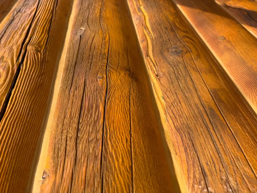 Close-up of weathered log home exterior showing deep grain texture, raised wood fibers, and surface erosion from improper pressure washing — the soft spring wood has been carved away between harder growth rings