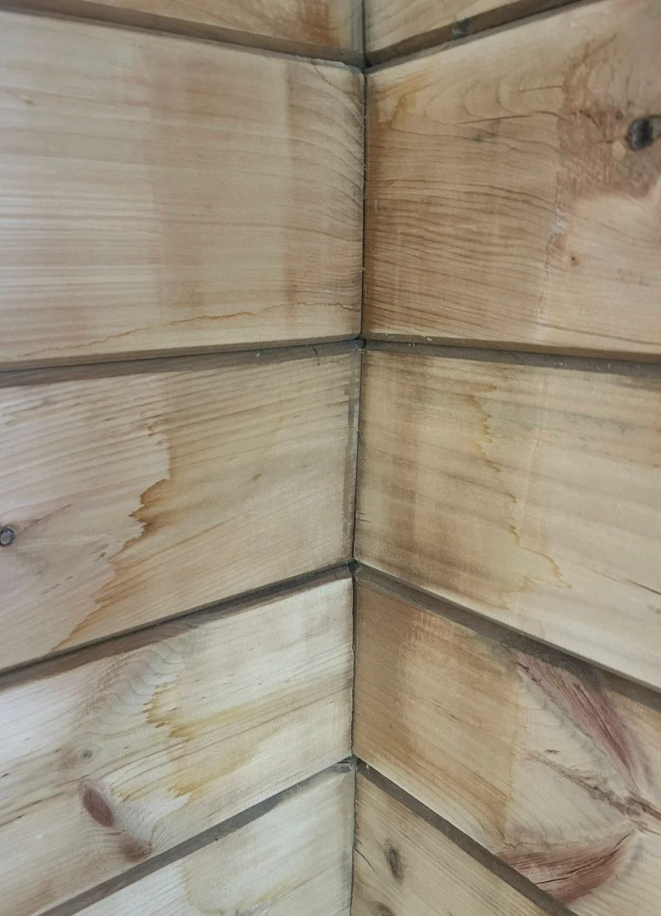 D-log corner joint showing amber-colored water stain runs dripping down between the flat-milled interior log faces, with visible staining at each horizontal joint