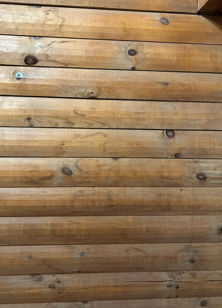 D-log interior wall showing extensive water stain discoloration across multiple flat-milled log faces, with darker bands of tannin bleeding visible at each horizontal joint between courses